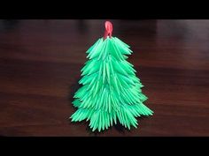 a green christmas tree made out of folded paper on a wooden table with a red ornament