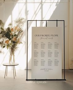 a wedding seating plan is displayed in front of a vase with flowers and greenery