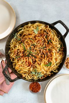 a skillet filled with pasta and sauce on top of a white table next to plates