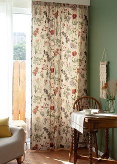 a living room with a table and chair next to a window covered in floral curtains