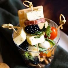 a glass filled with fruit and cheese on top of a green table cloth next to crackers