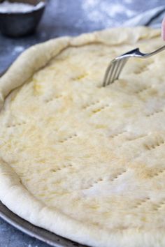 a person is using a fork to make an uncooked pizza crust on a baking sheet