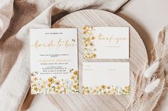 the wedding stationery is laid out on a wooden platter with flowers and greenery