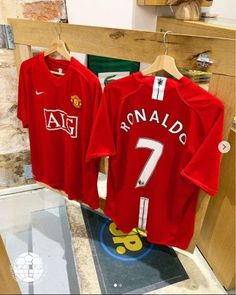 two red manchester united soccer shirts hanging on a rack