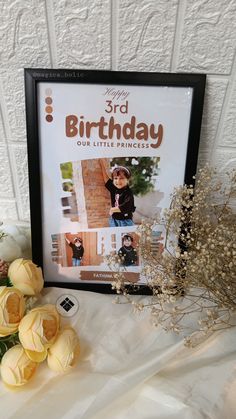 a birthday card and some flowers on a white tablecloth with a black framed photo