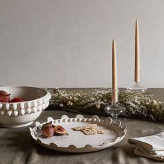 a table topped with plates and candles next to a bowl filled with fruit on top of a table