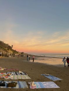 people are walking on the beach at sunset with blankets and towels laid out in front of them