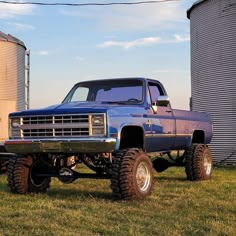 a large blue truck parked next to a silo on top of a grass covered field