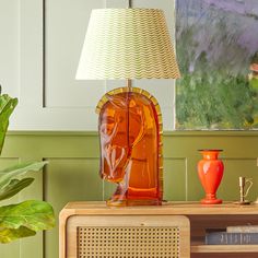 an orange vase sitting on top of a wooden table next to a lamp and painting