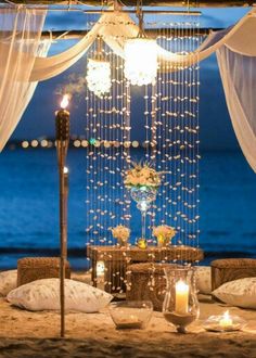 a table set up with candles, flowers and chandelier on the beach at night