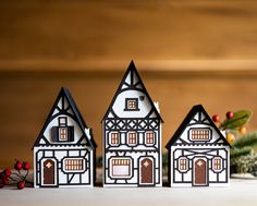 three paper houses sitting on top of a table next to christmas decorations and holly branches