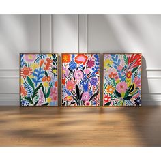 three colorful paintings on a wooden floor in front of a wall with white paneling