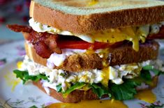 a sandwich with bacon, lettuce and cheese on it sitting on a plate