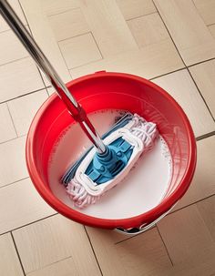 a red bucket with a mop in it on the floor next to a tile floor