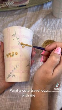 a woman is painting a cup with flowers on it