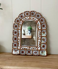 a decorative mirror sitting on top of a wooden shelf next to a potted plant