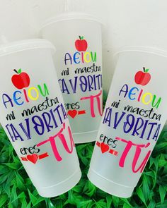 three plastic cups with writing on them sitting in some green grass and plants, one has an apple