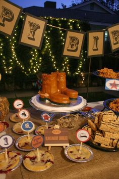 an outdoor dessert table with cookies, pies and other treats on it at night