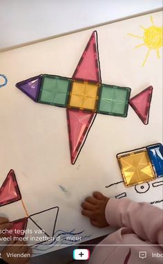 a child is drawing on a white board with colorful shapes and lines in the background