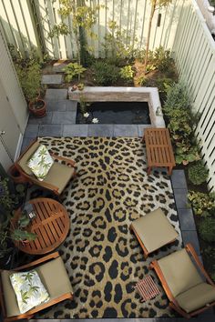 an outdoor living area with chairs, tables and a rug on the ground in front of a fence