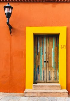 an orange building with a wooden door and light on the side walk next to it