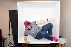 a woman with pink hair laying on top of a white box in front of a black backdrop