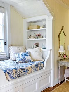 a white day bed sitting in front of a window next to a table with a lamp on it