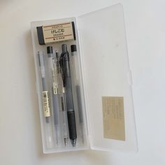 three pens in a plastic case on top of a white table next to an envelope