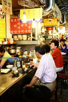 people sitting at tables in a restaurant with food on the counter and signs above them