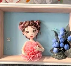 a doll is sitting on a shelf next to some blueberries and flowers in a frame