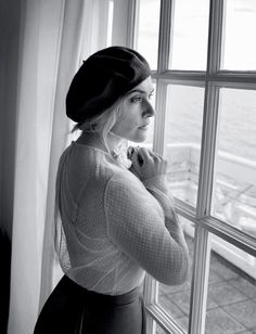 a woman standing by a window looking out at the ocean in black - and - white