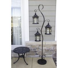 an iron lamp post with three lanterns on it's sides and a small table in front of the door