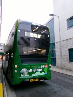 a green bus is parked on the side of the road next to a building and sidewalk