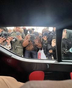 a group of people are taking pictures in the car's rear view mirror, with cameras around them