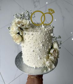 there is a wedding cake with two rings on top and flowers in the bottom tier