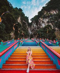 a woman sitting on top of colorful steps in front of a mountain with lots of stairs