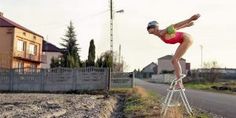 a woman standing on top of a ladder in the middle of a field next to a road