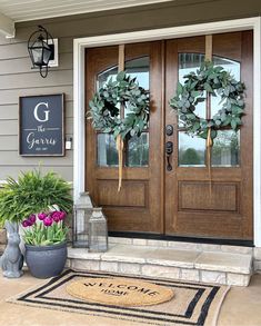 two wreaths on the front door of a house with flowers and plants in pots