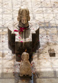 a small statue sitting on top of a fountain with flowers in it's mouth