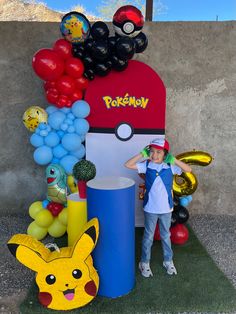 a young boy standing next to a fake pikachu and balloon display in front of a wall