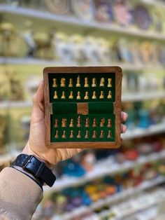 a person holding up a wooden chess board in front of shelves filled with other items