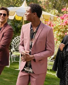 two men in suits standing next to each other on the grass with pink flowers behind them