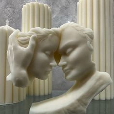 two white candles sitting next to each other on top of a glass table with a couple's head in between them