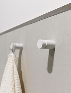 two white towels hanging on the wall next to a towel rack and toilet paper dispenser