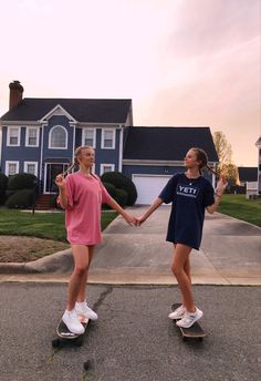 two girls on skateboards holding hands in front of a house