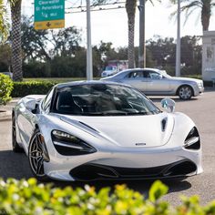 a white sports car parked in front of a parking lot with palm trees behind it