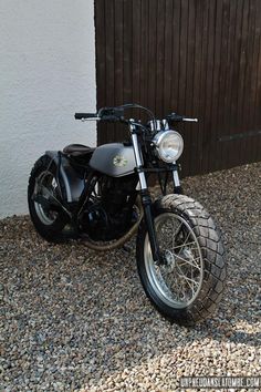 a black motorcycle parked in front of a wooden fence with gravel on the ground next to it