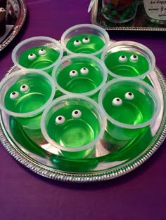 there are many green cups with googly eyes in them on the table next to other plates