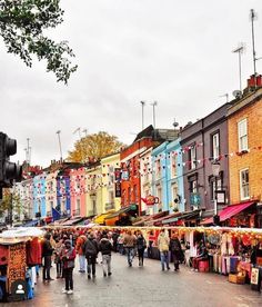 people are walking through an open air market on a rainy day in front of colorful buildings