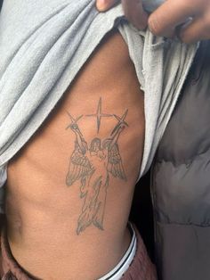 a person with a cross and angel tattoo on their side ribcage is holding a cell phone